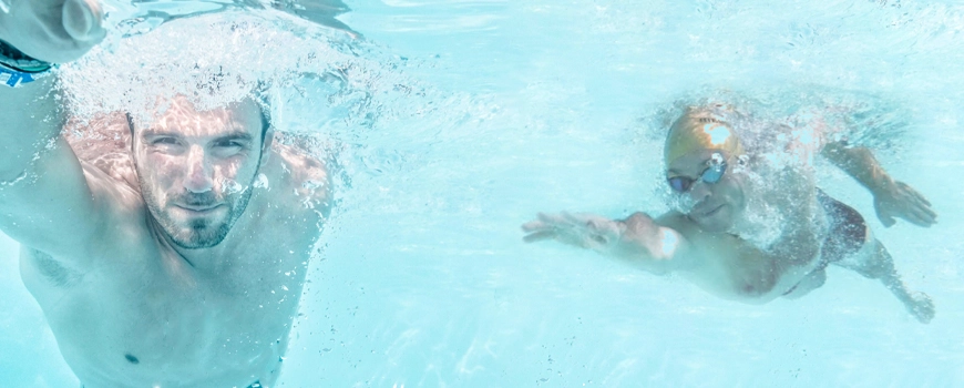 homens a nadar debaixo de água numa piscina.